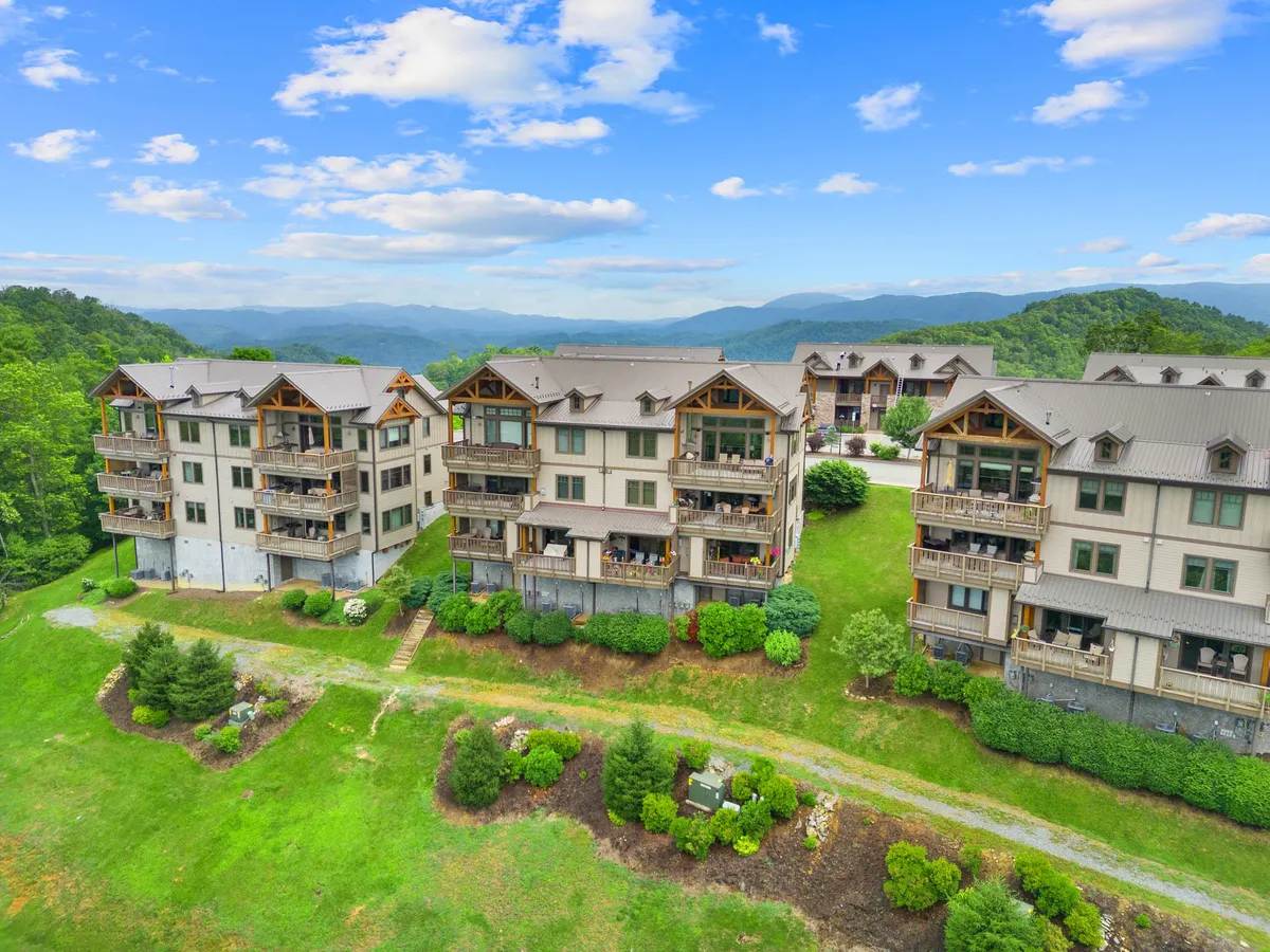 Multi-story buildings with balconies overlook green landscaping and a dramatic mountain backdrop. The image suggests opportunities for relaxing outdoors, exploring trails, and soaking up views.