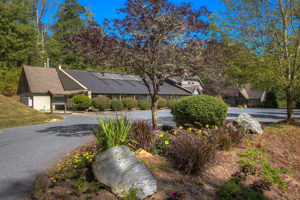 A well-maintained main building is surrounded by vibrant landscaping, trees, and flower beds. The scene exudes a welcoming and tranquil vibe, offering a glimpse into the resort’s communal areas and outdoor amenities, with nature integrated seamlessly into the design.