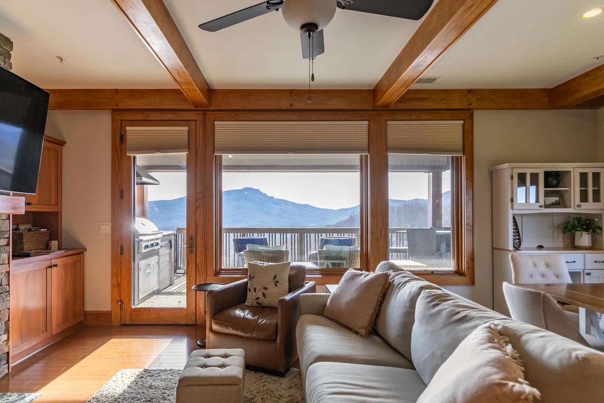 A bright and airy living and dining area with large windows offering panoramic mountain views, a comfy sofa, a dining table, and a well-equipped kitchenette. The scene highlights both relaxation and the enjoyment of meals with a scenic backdrop.