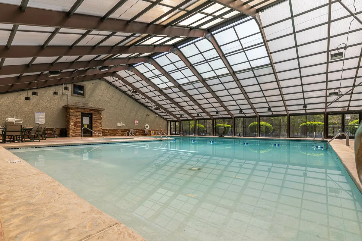 A bright indoor swimming pool is visible beneath a glass ceiling, with a seating area alongside. The tranquil atmosphere suggests relaxation and year-round enjoyment, regardless of the weather outside.