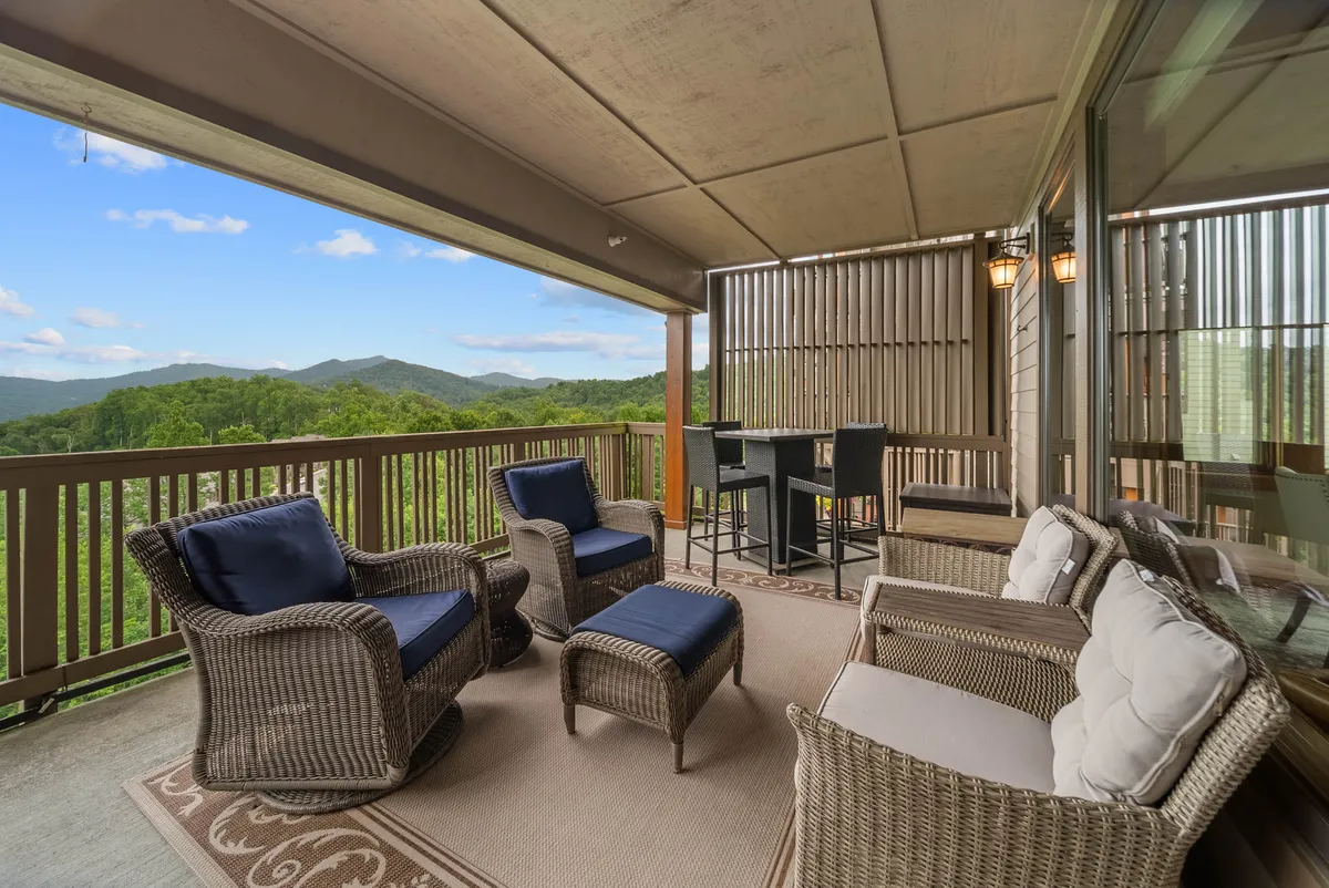 The image showcases a spacious outdoor deck with plush, comfortable seating and a dining area, all overlooking a sweeping, panoramic view of Grandfather Mountain. The scene is bathed in soft natural light, suggesting the perfect spot to relax, dine al fresco, or unwind with friends and family while immersed in the serene beauty of the mountains.