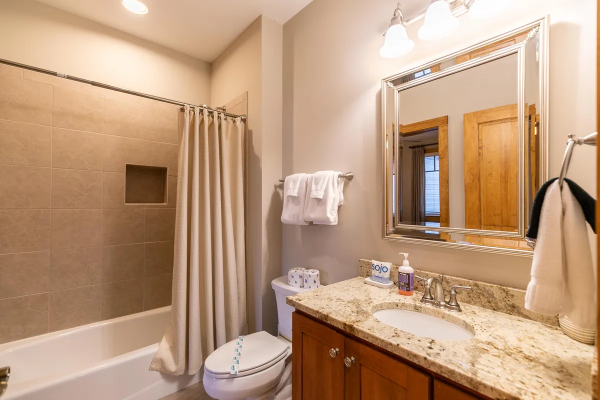 A bright and elegantly appointed bathroom featuring a bathtub, vanity with stone countertop, large mirror, and wooden cabinetry. The space is serene and functional, well-suited for relaxation and daily routines.