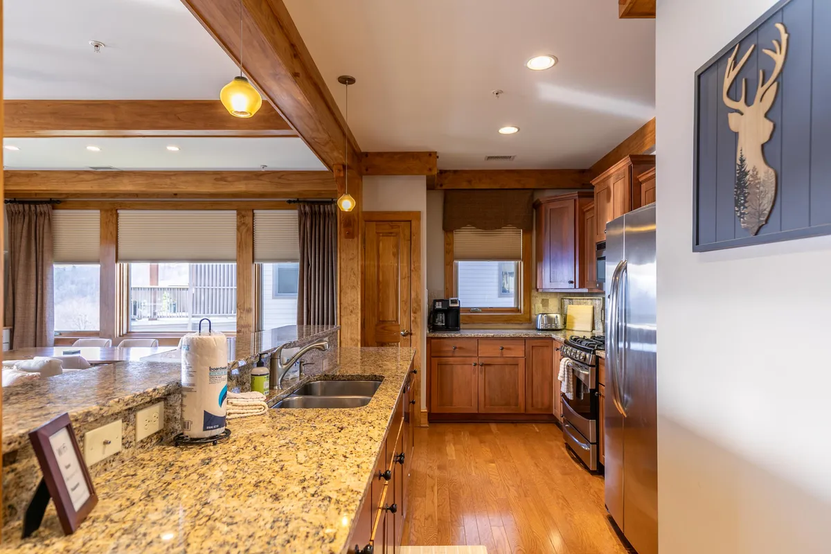 A cozy, stylish kitchen with granite countertops, warm wooden cabinetry, stainless steel appliances, and decorative artwork. The space is designed for both meal preparation and social interaction, with plenty of room for cooking and connecting.