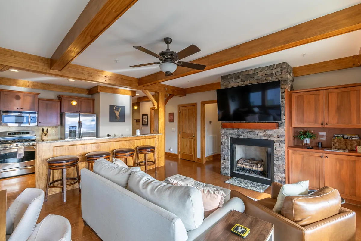 A cozy, open-plan living space featuring a stone fireplace, kitchen island, and comfortable sofa. The scene is well-lit and inviting, with modern fixtures and a layout that promotes relaxation and easy living.